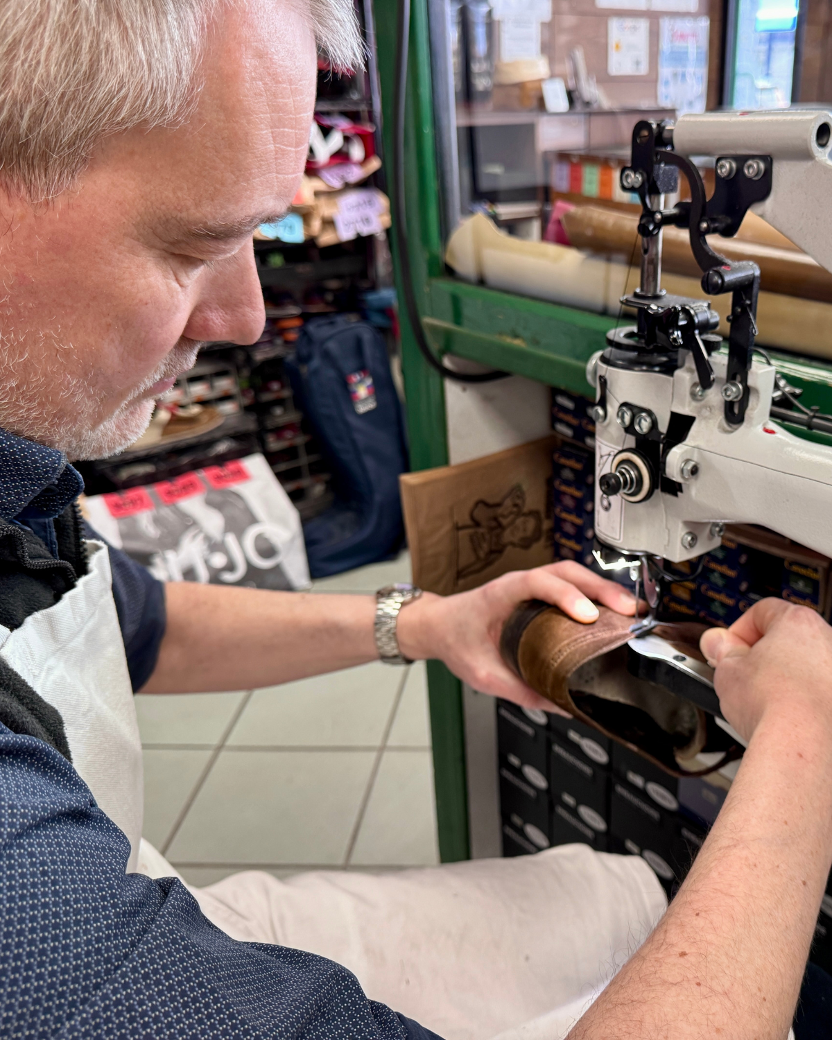 Hugo en train de coudre à la machine traditionnelle une pièce de cuir brun à l'atelier